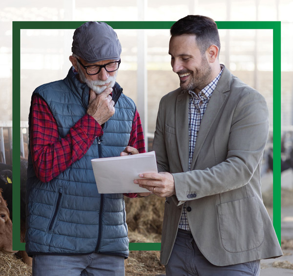 Two men reviewing paper documentation within a partially covered barn